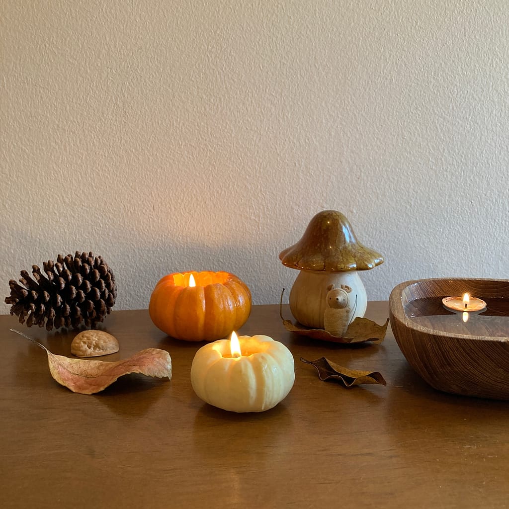 fall nature table with beeswax pumpkin candles, pinecone, walnut shell beeswax candles and a mouse.