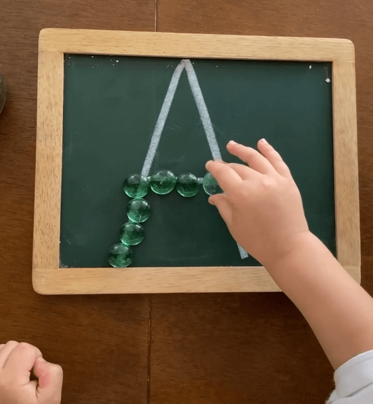 toddler using pincer grasp to pick up a marble on a chalkboard 